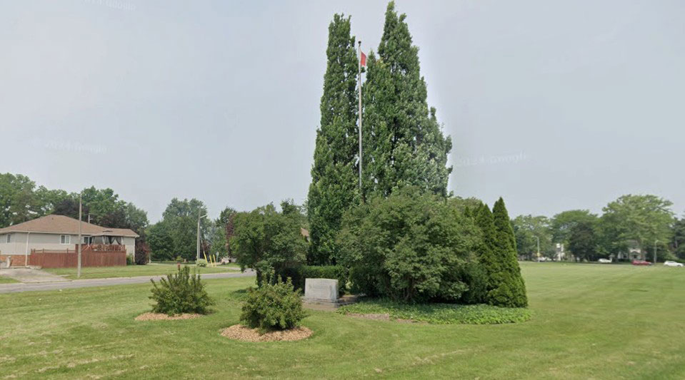 Street image of Stamford Green Park in summer showing mowed lawn and some shrubs.