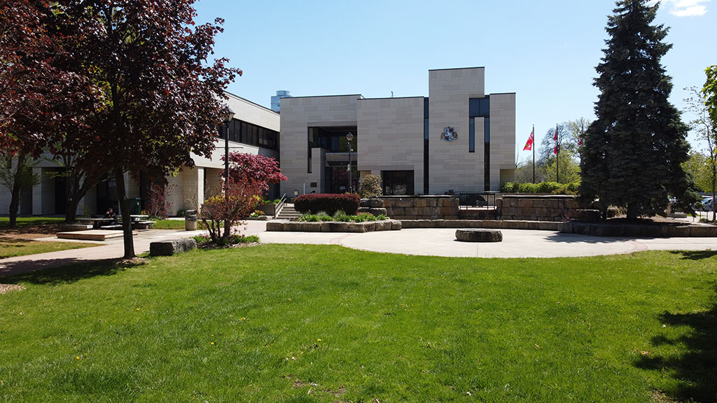 Front of City Hall showing the park area with green grass, the waterfall fountain in the background and surrounding trees and gardens.