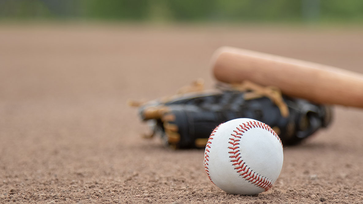 Close up of a baseball bat, glove and baseball on a dirt baseball field.