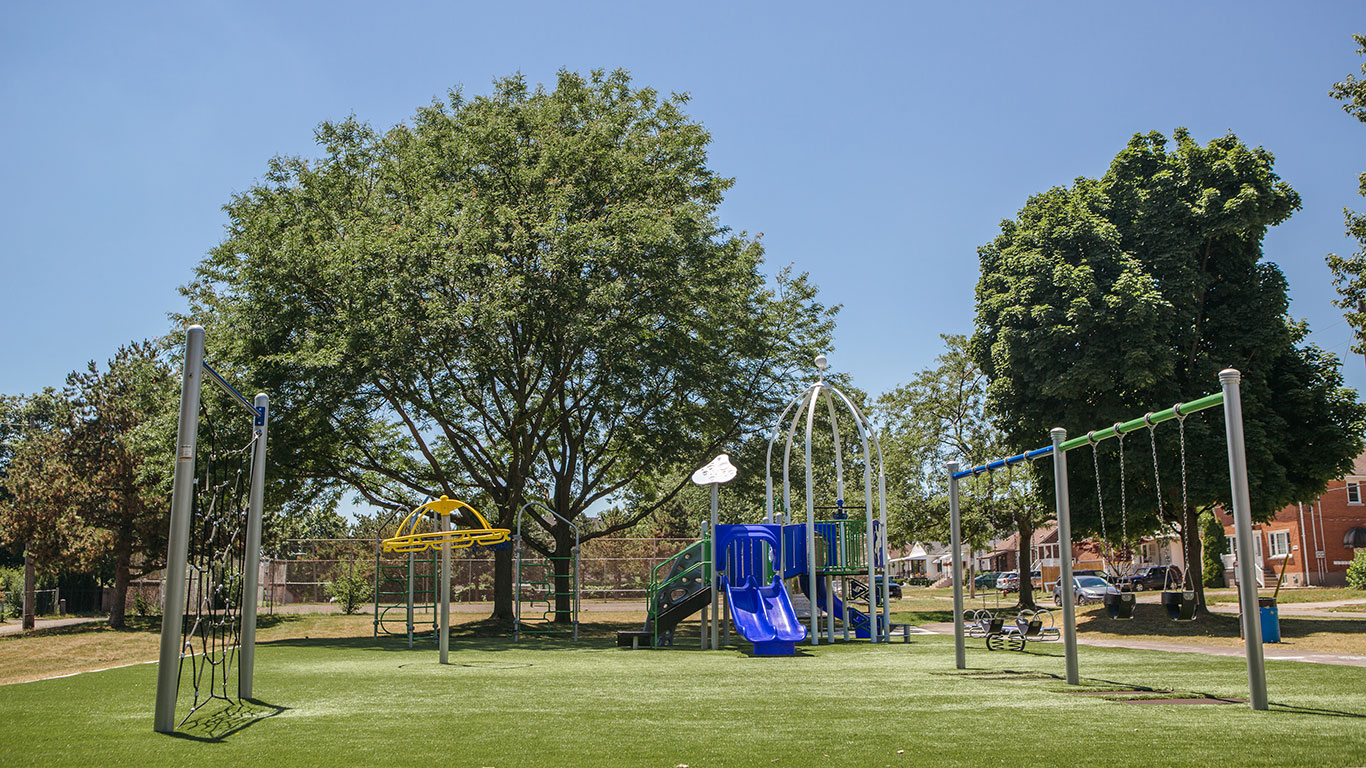 Ontario Park playground and swing set on green turf with a few trees in the background.