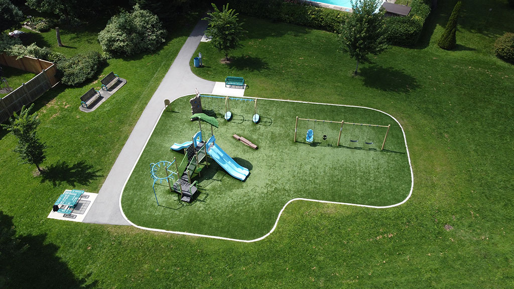 Drone overhead photo of Brookfield park playground, park benches and walking path, surrounded by green grass.