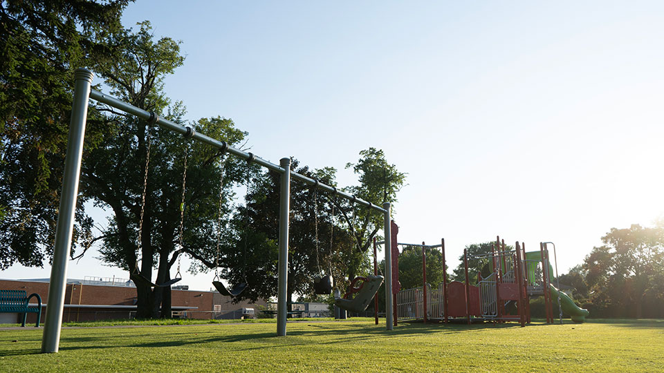 Photo of Cherryhill Park playground and swings, surrounded by green grass and trees. 