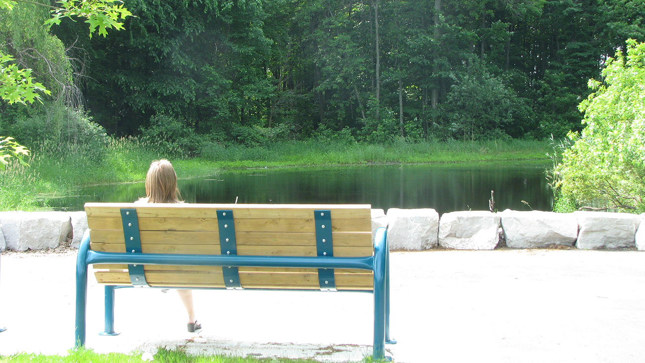 Woman sitting on a park bench in view of the natural water area.
