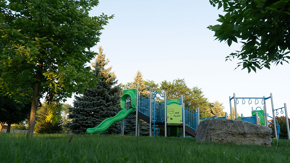 Playground and slide at Balmoral Park with green grass and mature trees.