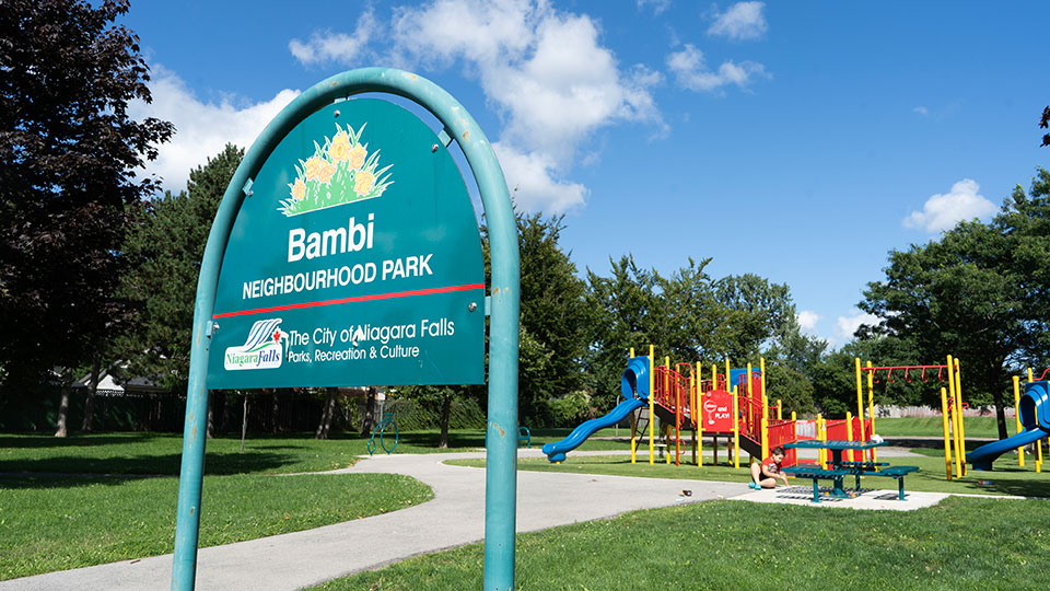 Playground at Bambi Park, also showing the park sign, picnic table, and walking path.